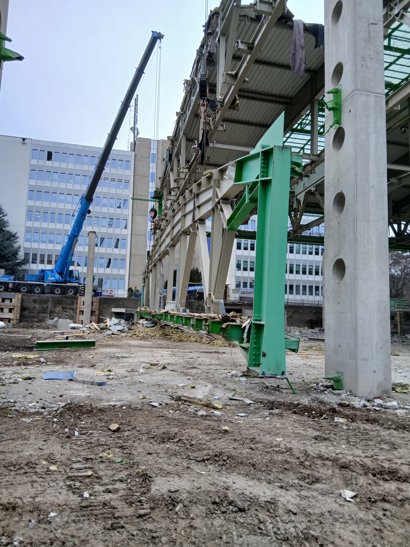 Grün beschichtete Stahlrahmen und Betonstützen auf der Abbruchfläche, Schutt und gelöste Träger.